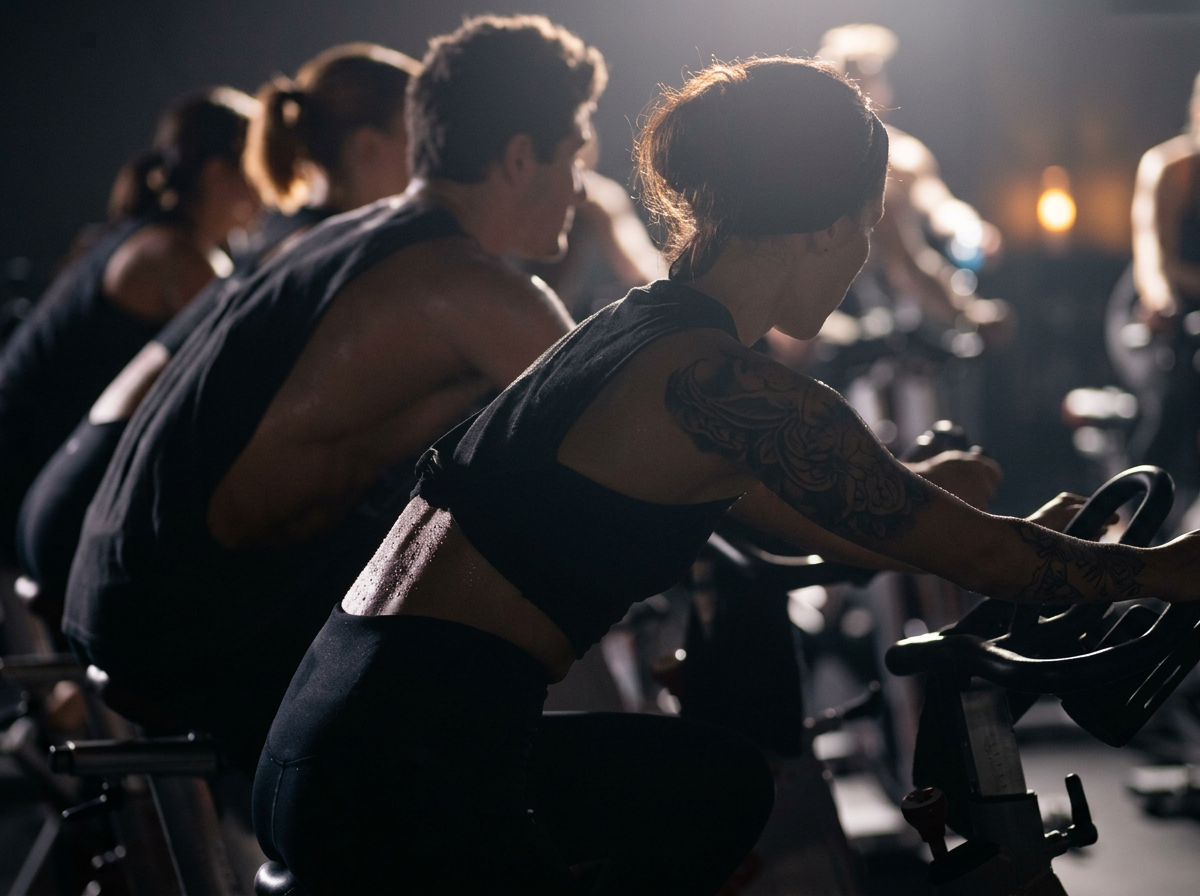 Members riding spin bikes side by side in the dim infrared studio